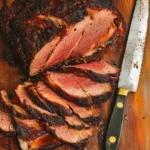 Sliced smoked beef roast with bark and smoke ring on cutting board.